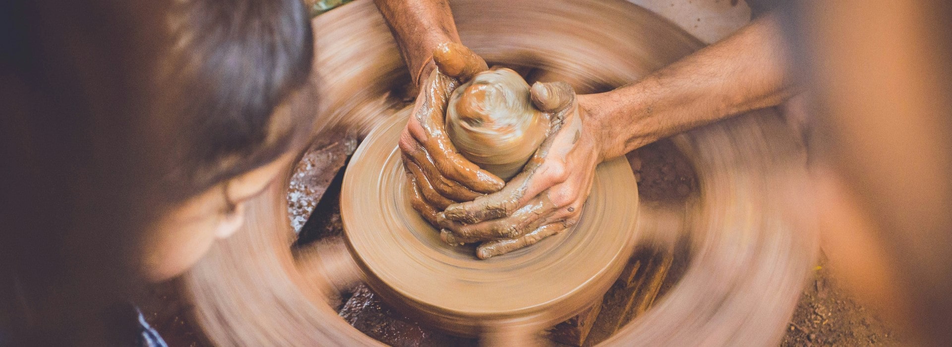 A young girl is watching a ceramic artisan creating a piece in clay